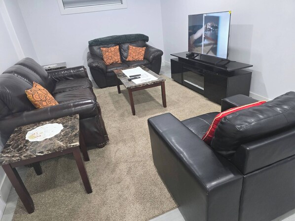A living room with two black leather sofas, a coffee table, and a flat-screen TV. - Cy Becker Drive 2023 Luxury Home (Edmonton)