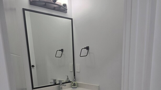 A bathroom with a white sink, mirror, and towel rack. - Cy Becker Drive 2023 Luxury Home (Edmonton)