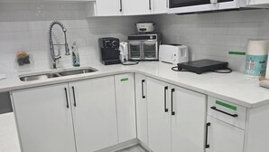 A modern kitchen with white cabinets, a stainless steel sink, a microwave, a toaster, and a coffee maker. - Cy Becker Drive 2023 Luxury Home (Edmonton)