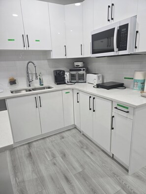 A modern kitchen with white cabinets, a stainless steel sink, a microwave, a toaster, and a coffee maker. - Cy Becker Drive 2023 Luxury Home (Edmonton)