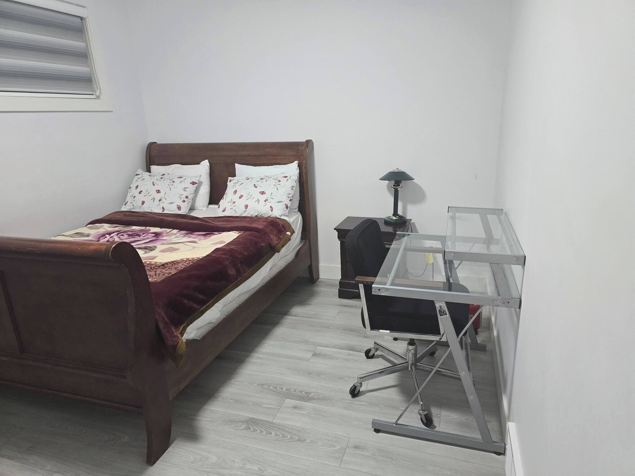Een slaapkamer met een houten bed, een bureau met een lamp en een overzichtelijke bureaustoel.