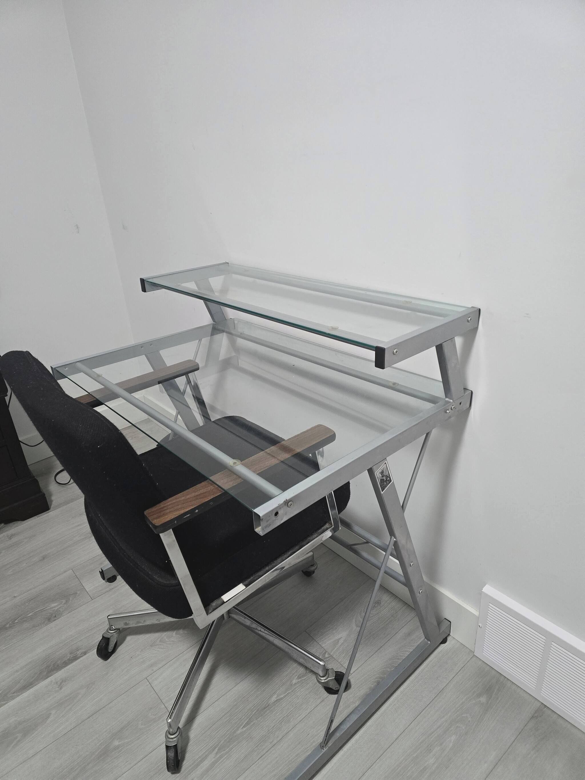 Un escritorio de metal con superficie de vidrio y una silla de oficina negra.