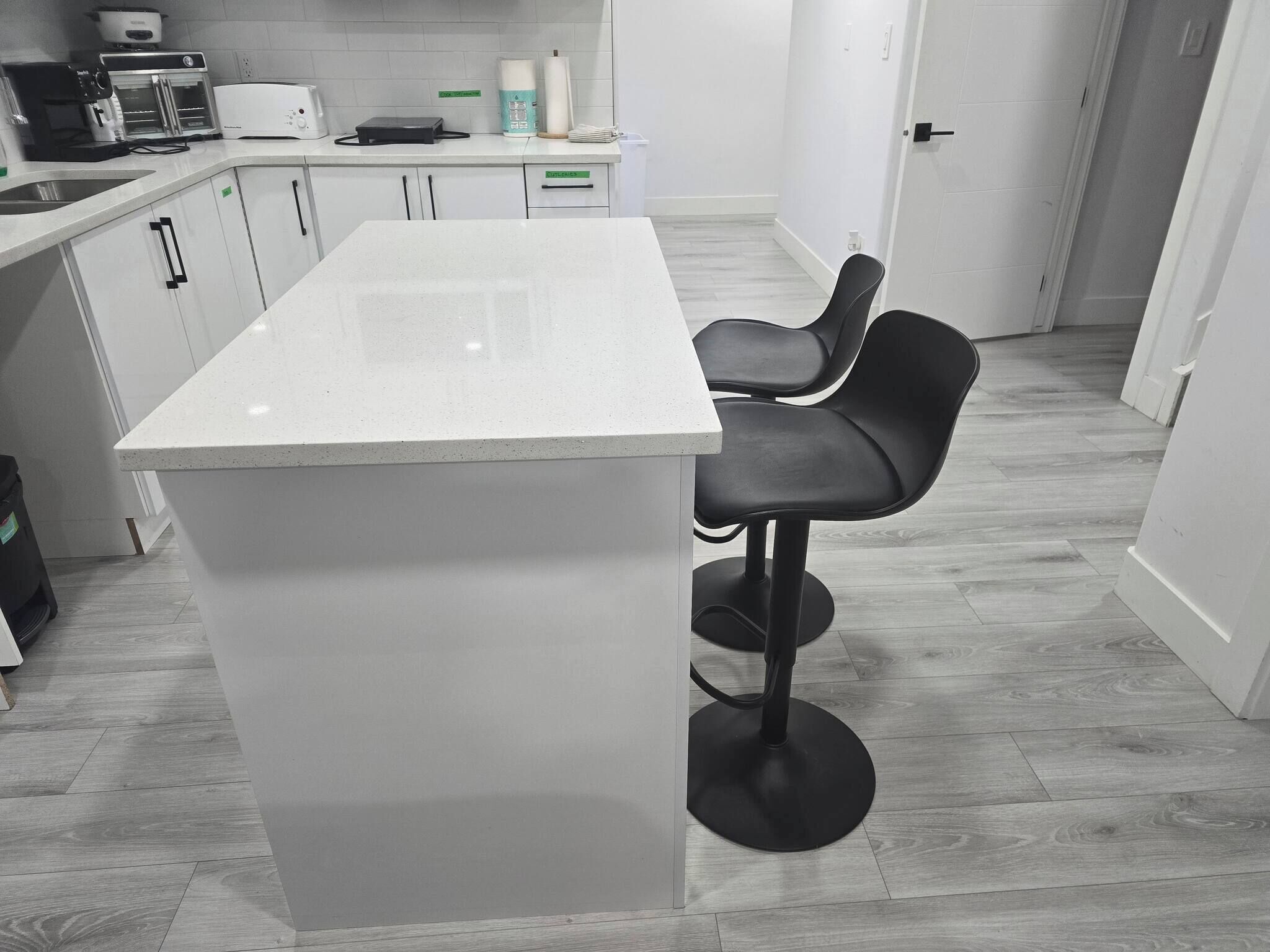 A modern kitchen with a white countertop, black bar stools, and various appliances.