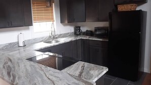 A modern kitchen with dark cabinets, a black refrigerator, and a marble countertop.