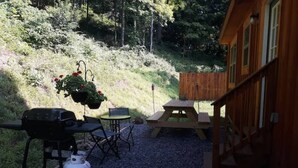 A wooden cabin with a gravel patio, a barbecue grill, a picnic table, and a hanging flower pot.