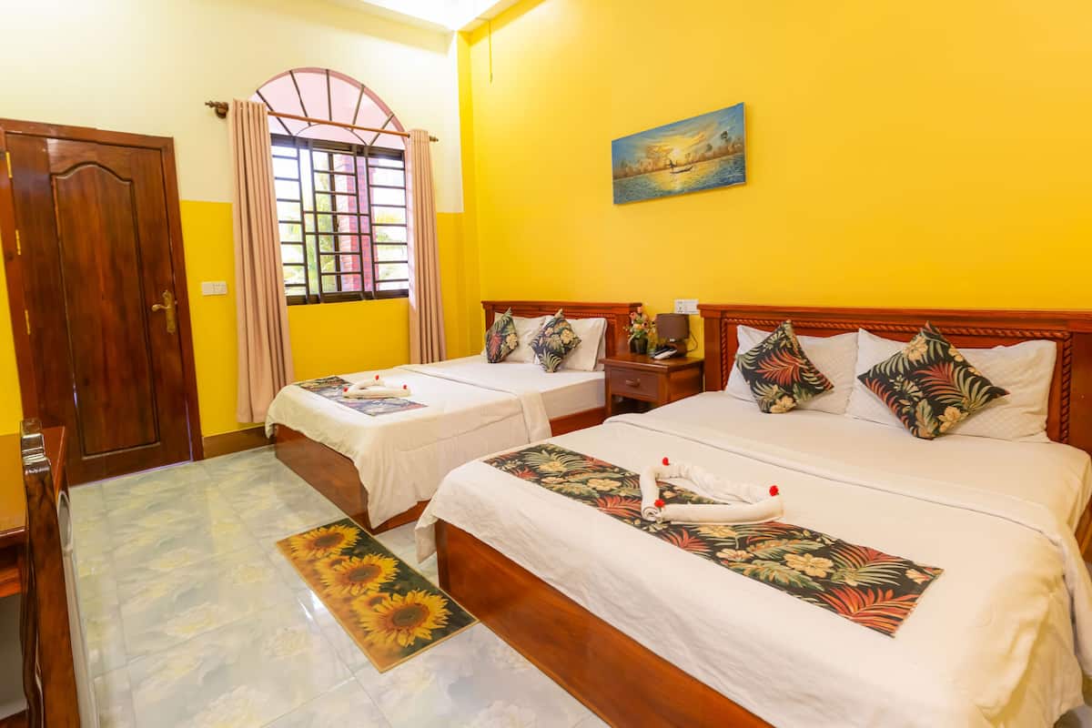 A hotel room with two beds, a wooden door, a window with curtains, a painting on the wall, and a floral rug.