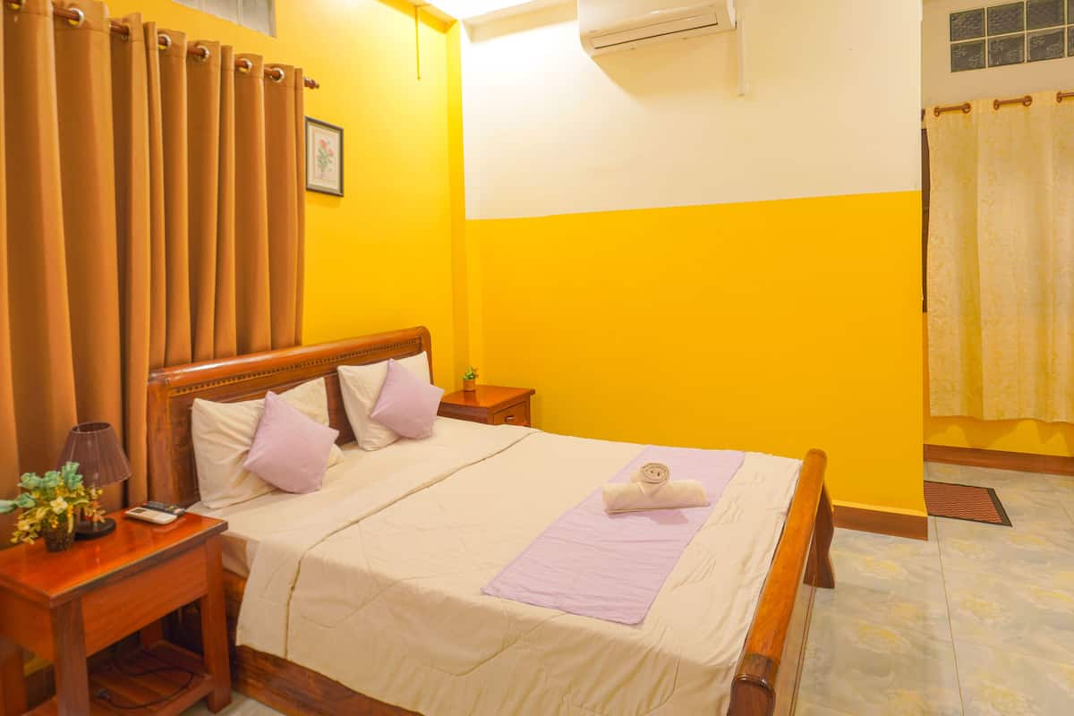 A hotel room with a bed, wooden headboard, two bedside tables, a nightstand, a lamp, and a window with curtains.