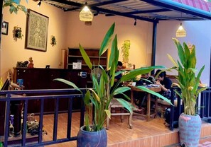 Et indendørs siddeområde med borde og stole omgivet af plantekasser.