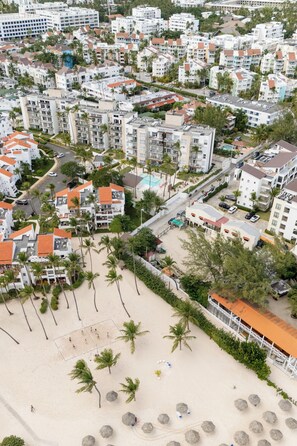 Vue aérienne d’une zone résidentielle côtière, avec de nombreux immeubles d’appartements, une plage de sable et des palmiers.