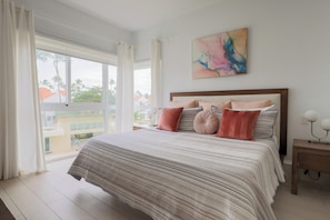 Une chambre avec un grand lit, une table de chevet, une lampe fixée au mur et une fenêtre avec des rideaux.