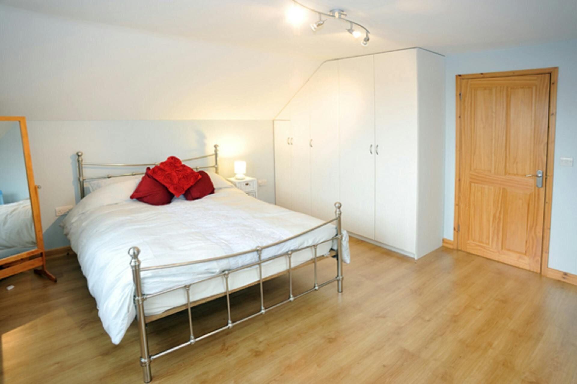 A bedroom with a metal-framed bed, white bedding, a wooden wardrobe, and a wooden door.