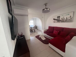 Ein Wohnzimmer mit rotem Sofa, einem an der Wand befestigten Fernseher und einem Essbereich im Hintergrund.