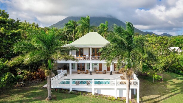 A two-story house with a green roof, surrounded by lush greenery and palm trees. - Saddle Hill View Villa (Charlestown)