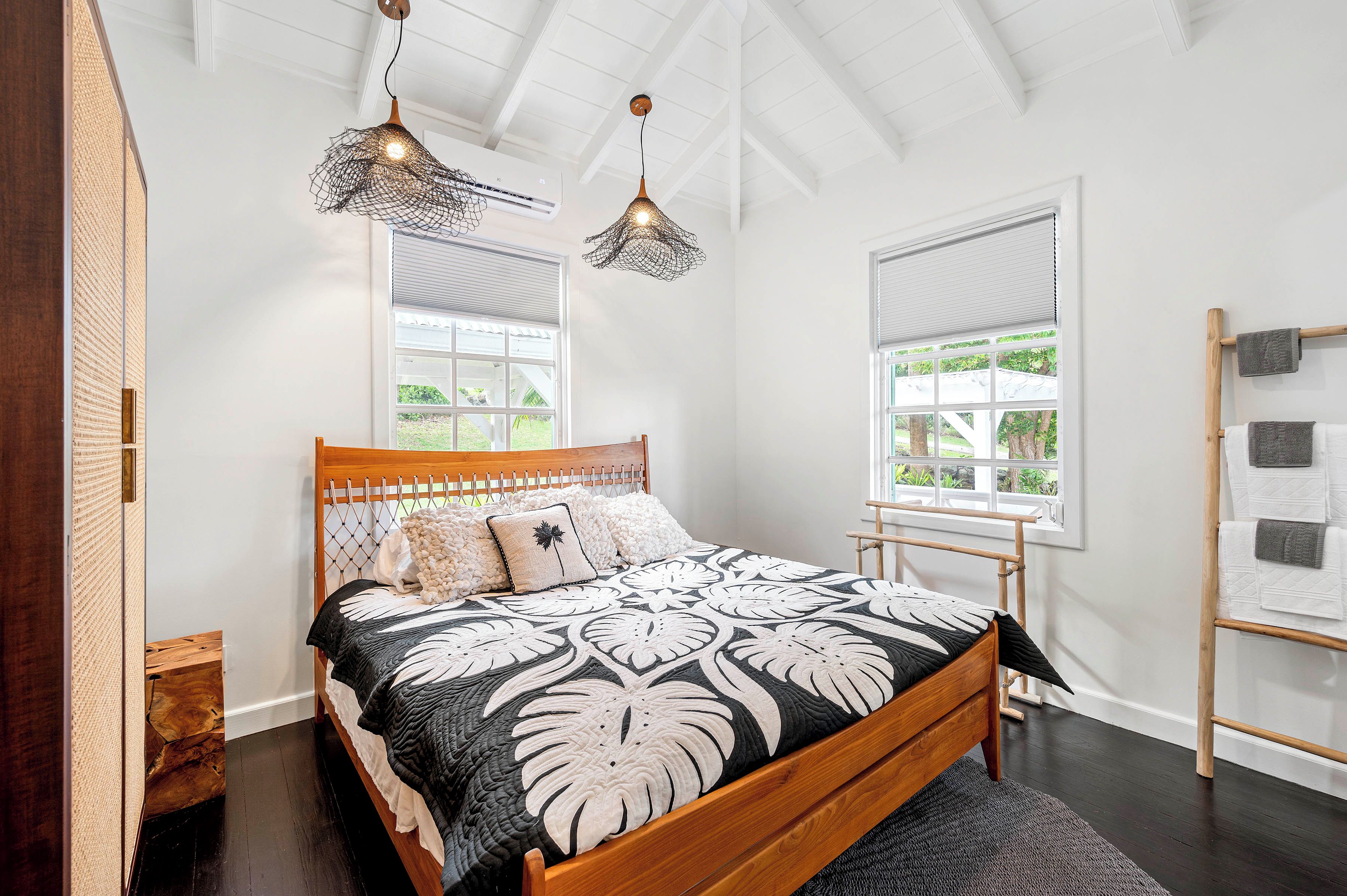 A bedroom with a wooden bed, two hanging light fixtures, a window with blinds, and a wooden ladder against the wall.