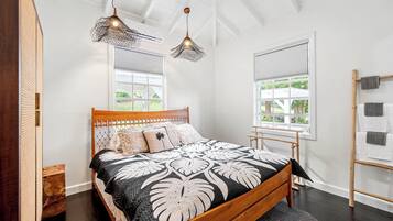 A bedroom with a wooden bed, two hanging light fixtures, a window with blinds, and a wooden ladder against the wall.