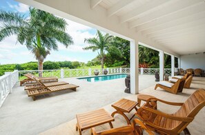 A covered outdoor area with wooden lounge chairs and a pool. - Saddle Hill View Villa (Charlestown)