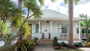 A white building with green shutters, a porch, and a stone statue. - Saddle Hill View Villa (Charlestown)