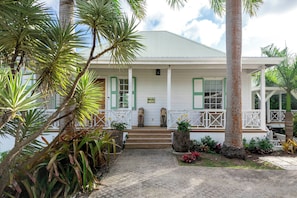 A white building with green shutters, a porch, and a stone statue. - Saddle Hill View Villa (Charlestown)