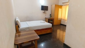 A small, clean room with a bed, a wooden table, a TV mounted on the wall, and a wardrobe. - Stayz Royale Mysuru - Near Mysuru Palace (Mysore)