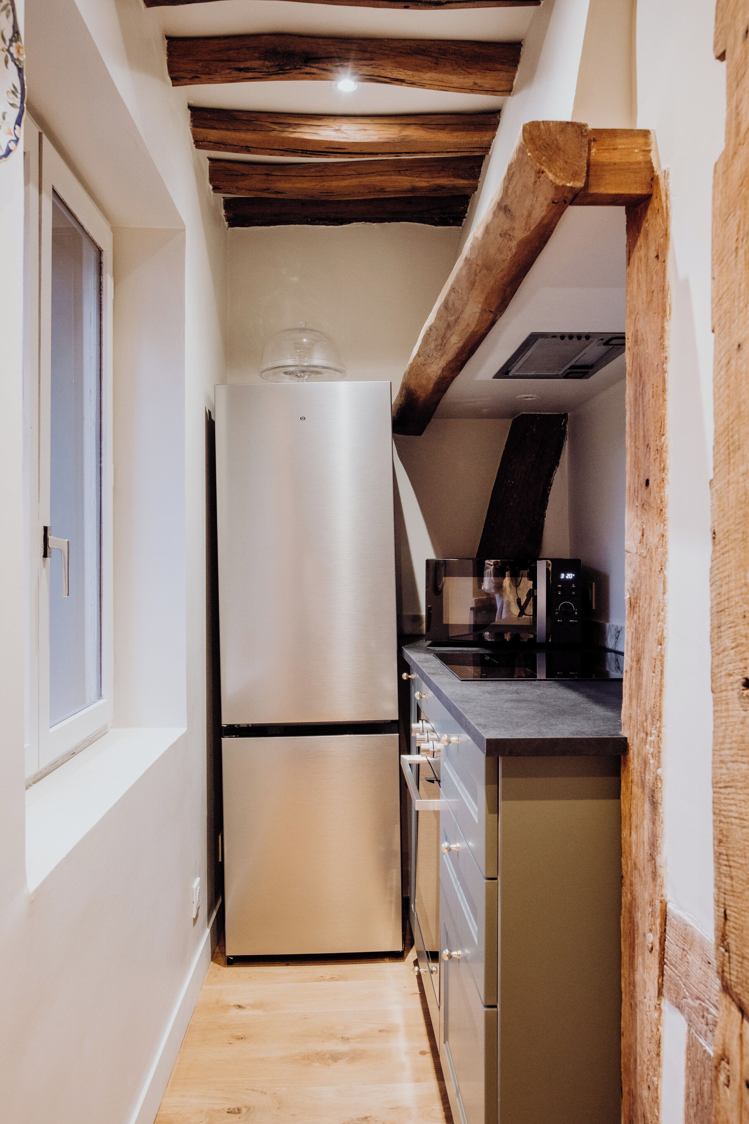 Eine schmale Küche mit einem Edelstahlkühlschrank, einer Mikrowelle und Holzbalken an der Decke.