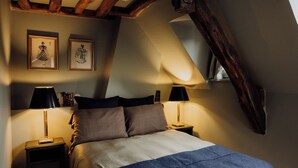 A bedroom with a sloped ceiling, two bedside lamps, a bed with a blue blanket, and two framed pictures on the wall. - Le Cotin Bleu. Duplex. Old Market. Sleeps 4/6 (Rouen)