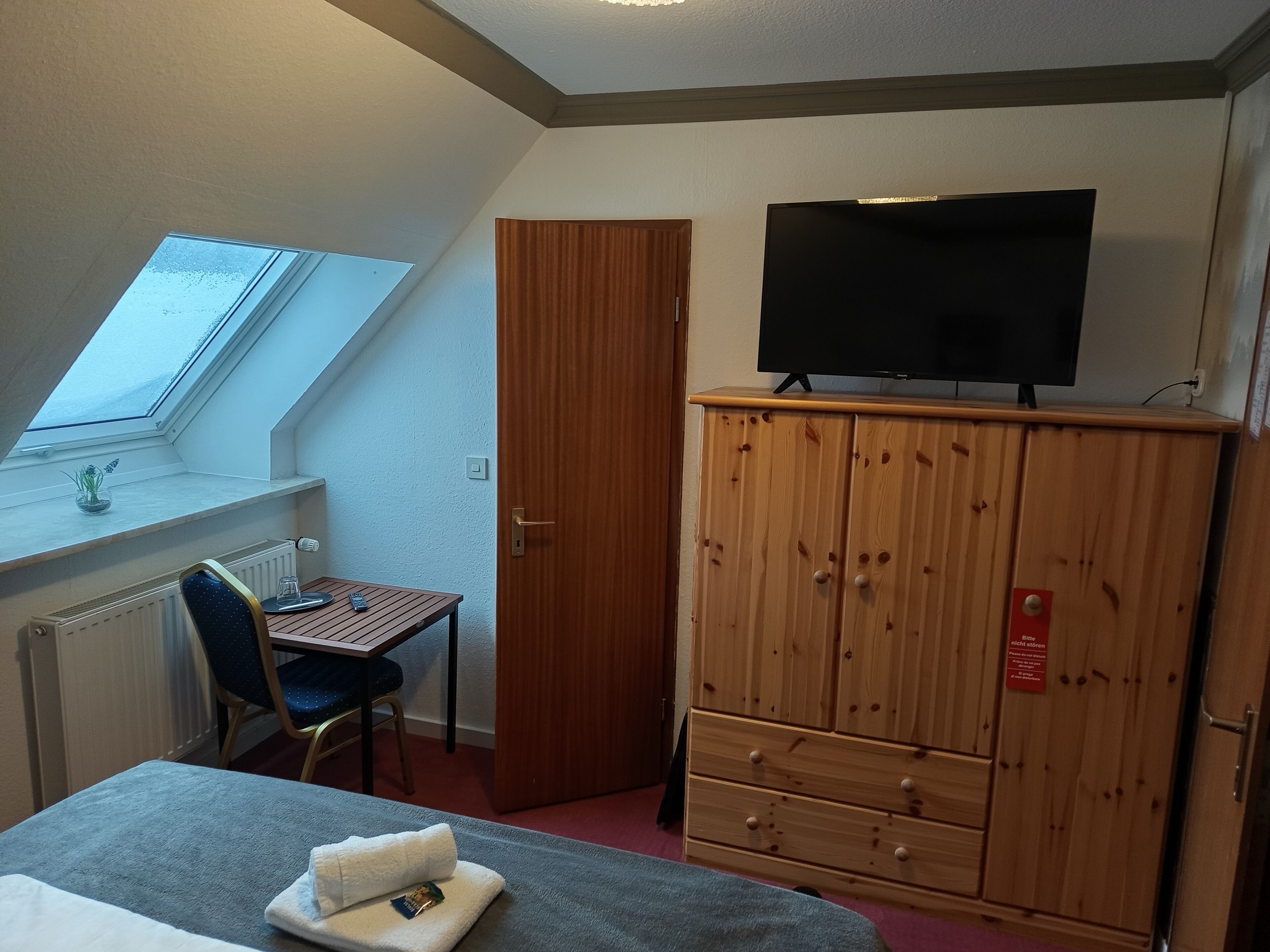 Ein Zimmer mit einem Bett, einem Schreibtisch mit Stuhl, einem Fernseher auf einer Holzkommode und einem Fenster mit Blick.