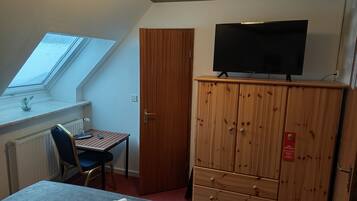 Ein Zimmer mit einem Bett, einem Schreibtisch mit Stuhl, einem Fernseher auf einer Holzkommode und einem Fenster mit Blick.