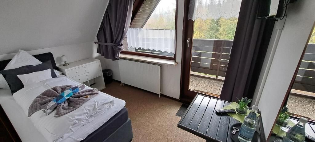 A bedroom with a bed, a small table with a water bottle, a radiator, and a window with curtains.