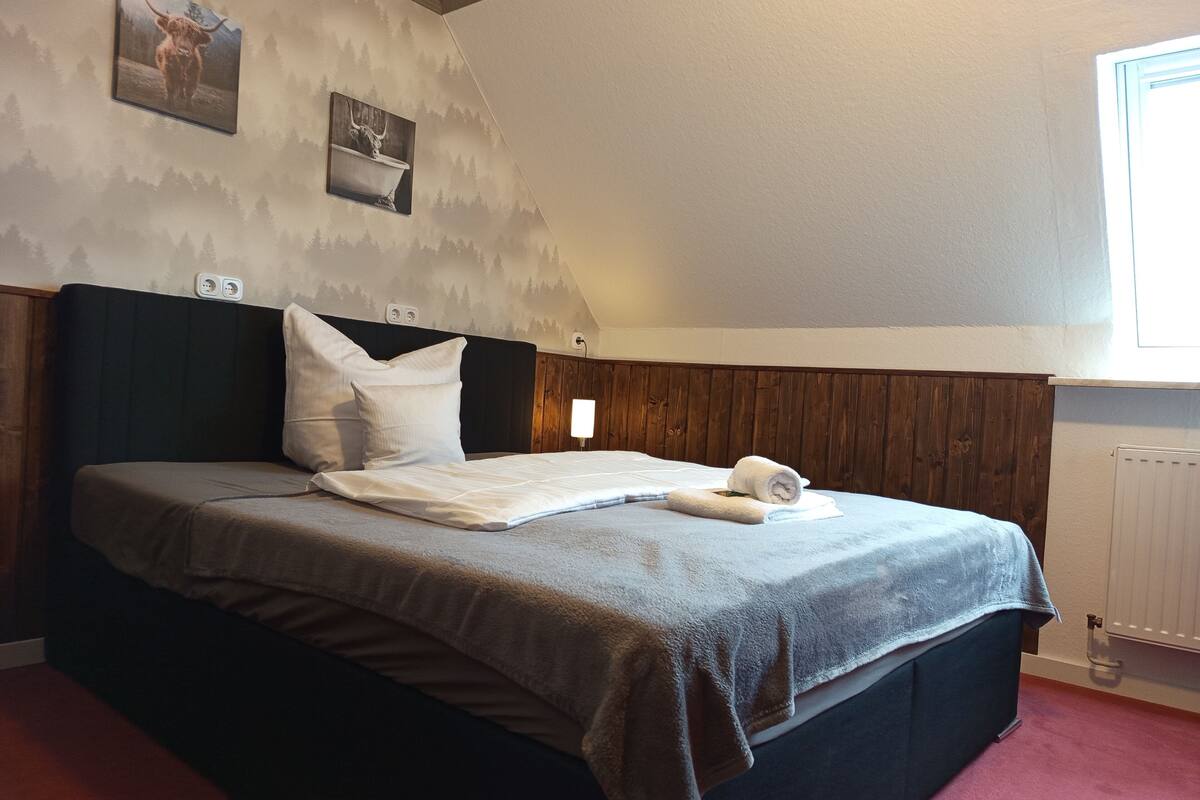 Une chambre à coucher avec un lit, une tête de lit, des œuvres d’art murales et une fenêtre.