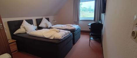 Ein Hotelzimmer mit zwei Betten, einem Schreibtisch und einem Fenster mit Blick auf Grünflächen.
