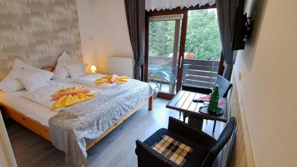 Een slaapkamer met een bed, een klein tafeltje met een stoel, en uitzicht op het omliggende landschap door een schuifdeur.