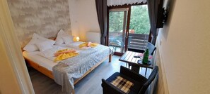 A bedroom with a bed, a small table with a chair, and a view of the outdoors through a sliding door. - Pension Quellenhof  (Altenau)