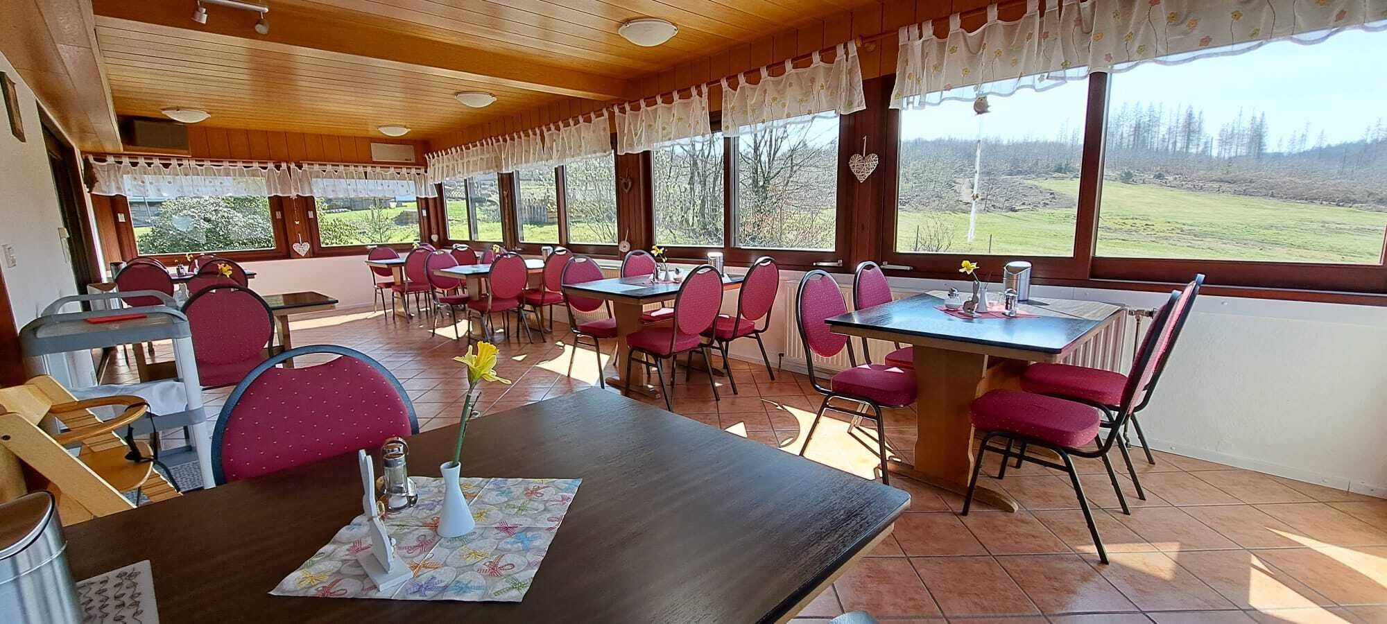 A restaurant with wooden interior, red chairs, and large windows offering a view of the countryside.