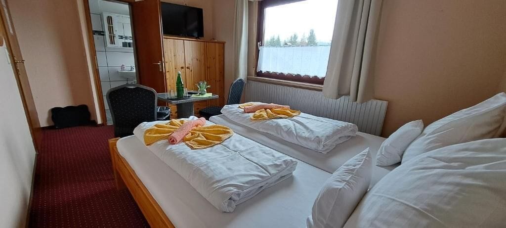 Une chambre d’hôtel avec deux lits, un bureau avec une chaise, une télévision et une fenêtre donnant sur l’extérieur.