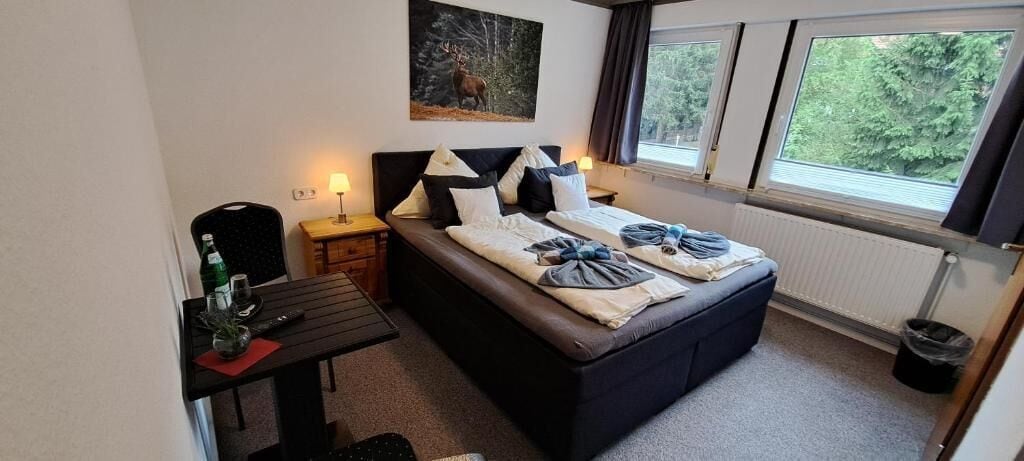 Ein Schlafzimmer mit Bett, Nachttischen, einem Schreibtisch und einem Fenster mit Blick auf Bäume.