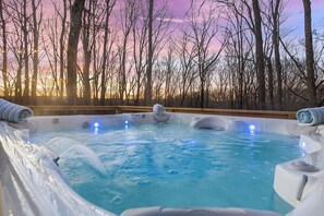 Een bubbelbad met jets, omringd door een houten terras en bomen, tegen een zonsondergang.