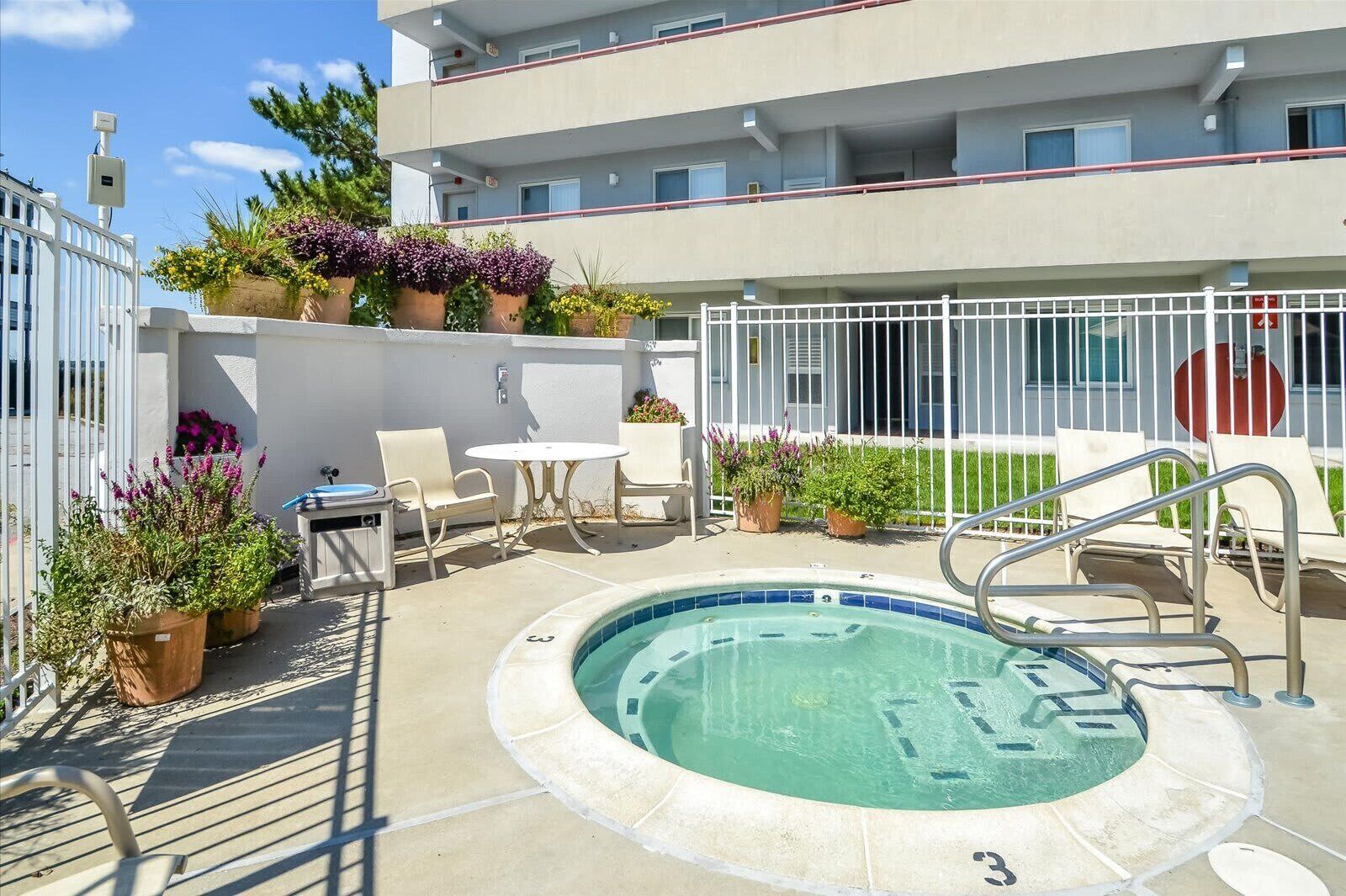 A pool area with a hot tub, lounge chairs, and potted plants.