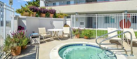 A pool area with a hot tub, lounge chairs, and potted plants.