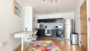 A compact kitchen with a washing machine, a microwave, and a refrigerator. - Modern 1-Bed Flat | Cardiff City Centre | Free Parking (Cardiff)