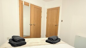 A bedroom with a bed, two wooden doors, and two folded towels on the bed. - Modern 1-Bed Flat | Cardiff City Centre | Free Parking (Cardiff)