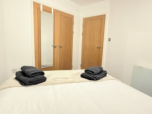 Une chambre à coucher avec un lit, deux portes en bois et deux serviettes pliées posées sur le lit.