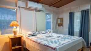 Ein Schlafzimmer mit einem Bett, einem Nachttisch, einer Lampe, einem Fenster mit Vorhängen und einer Klimaanlage.