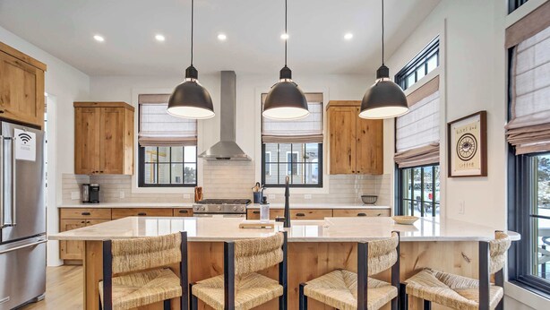 Una cocina moderna con armarios de madera, una isla central con taburetes altos, iluminación colgante y ventanas amplias.