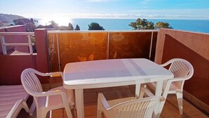 Una terraza con una mesa y cuatro sillas blancas, con vistas a la costa.