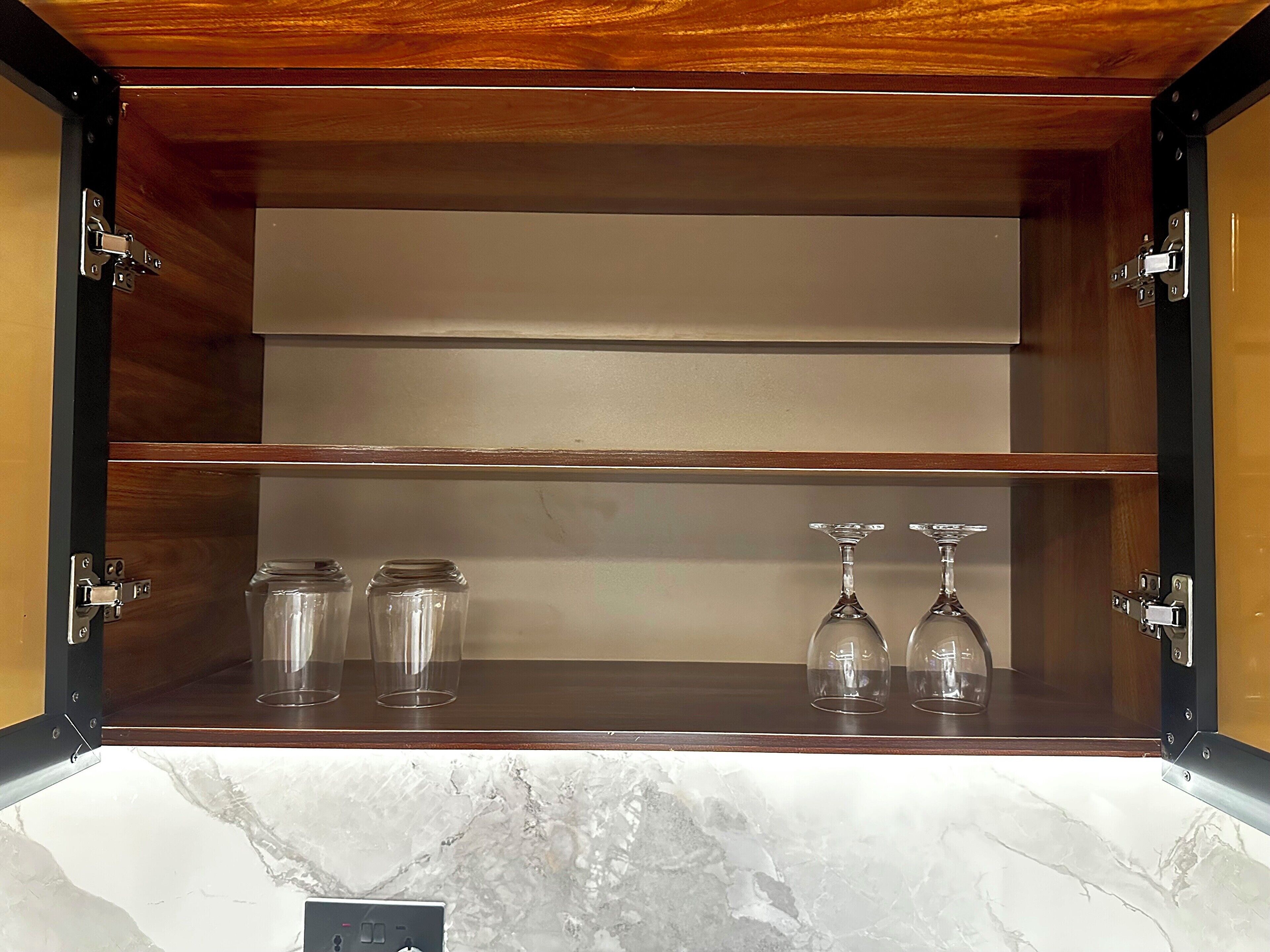 Un mueble de madera con tres estantes, cada uno con frascos de vidrio transparente y dos copas de vino.