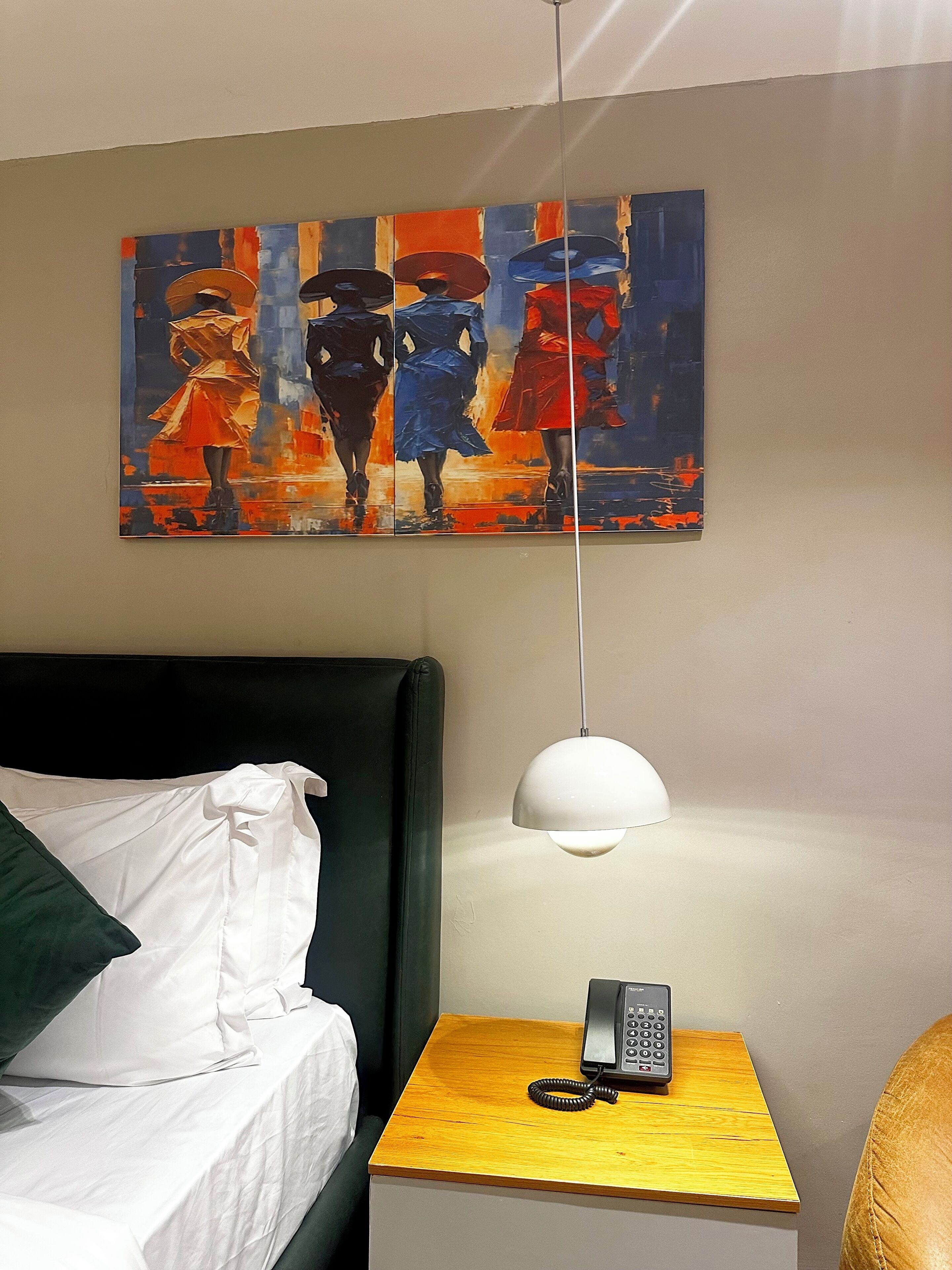 Habitación de hotel con una cama, una mesita de noche con lámpara, un cuadro en la pared y un teléfono sobre la mesa.