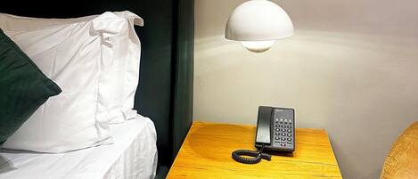 Habitación de hotel con una cama, una mesita de noche con lámpara, un cuadro en la pared y un teléfono sobre la mesa.