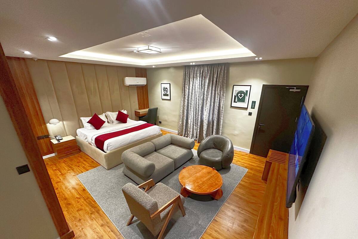 A modern hotel room with a bed, sofa, armchair, and a small round table.