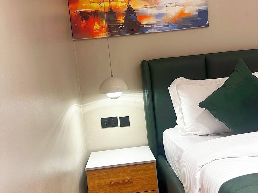 A hotel room with a bed, a nightstand with a lamp, a drawer, and a painting of the Eiffel Tower.