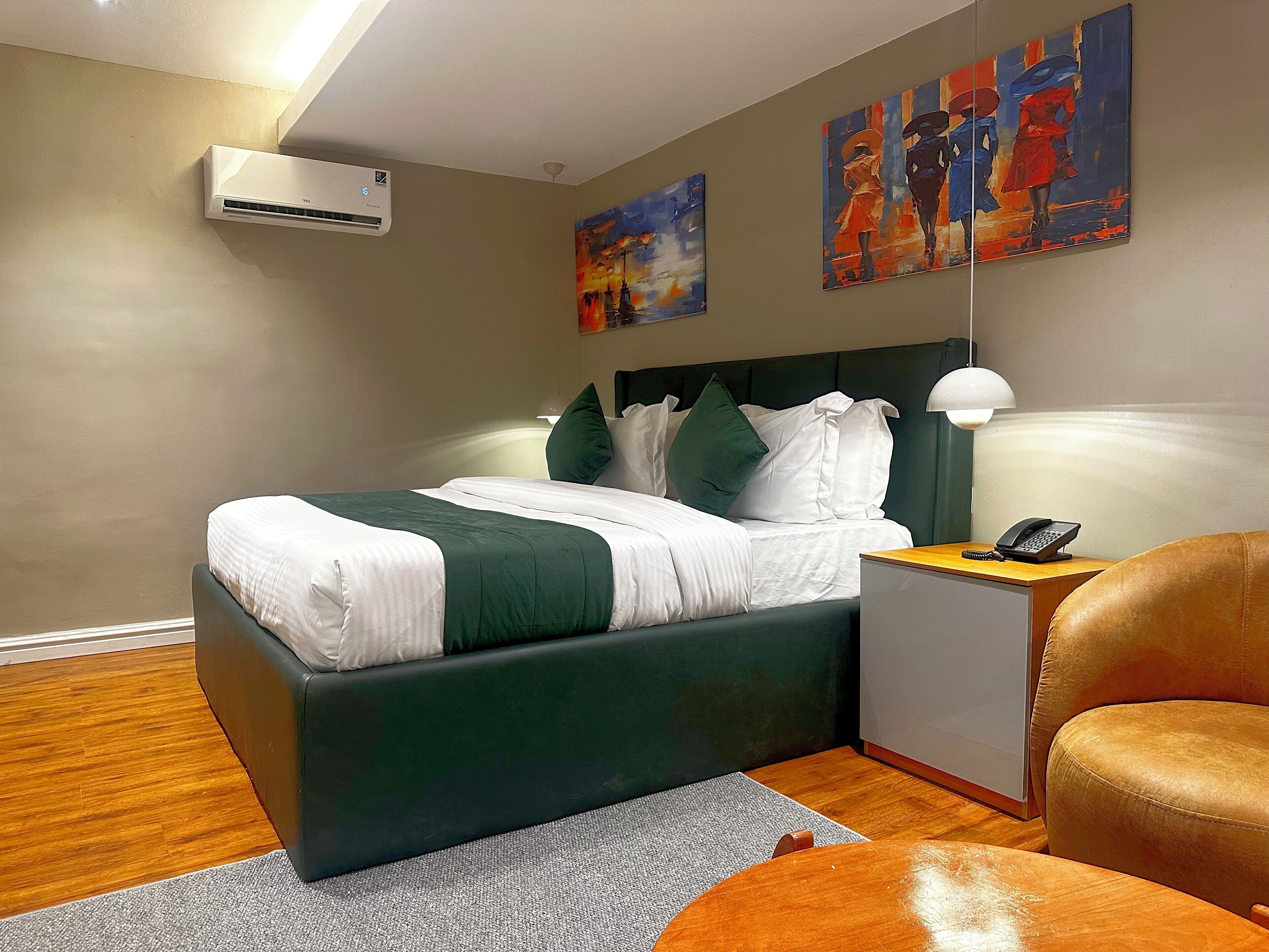 A hotel room with a bed, a side table with a phone, a chair, and artwork on the walls.